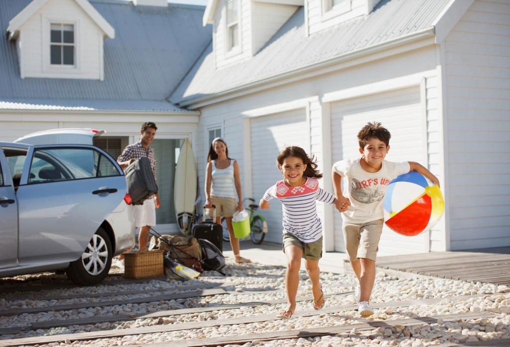A family happily unloading and playing outside their clean, white house, representing the joy and comfort of a well-maintained home.