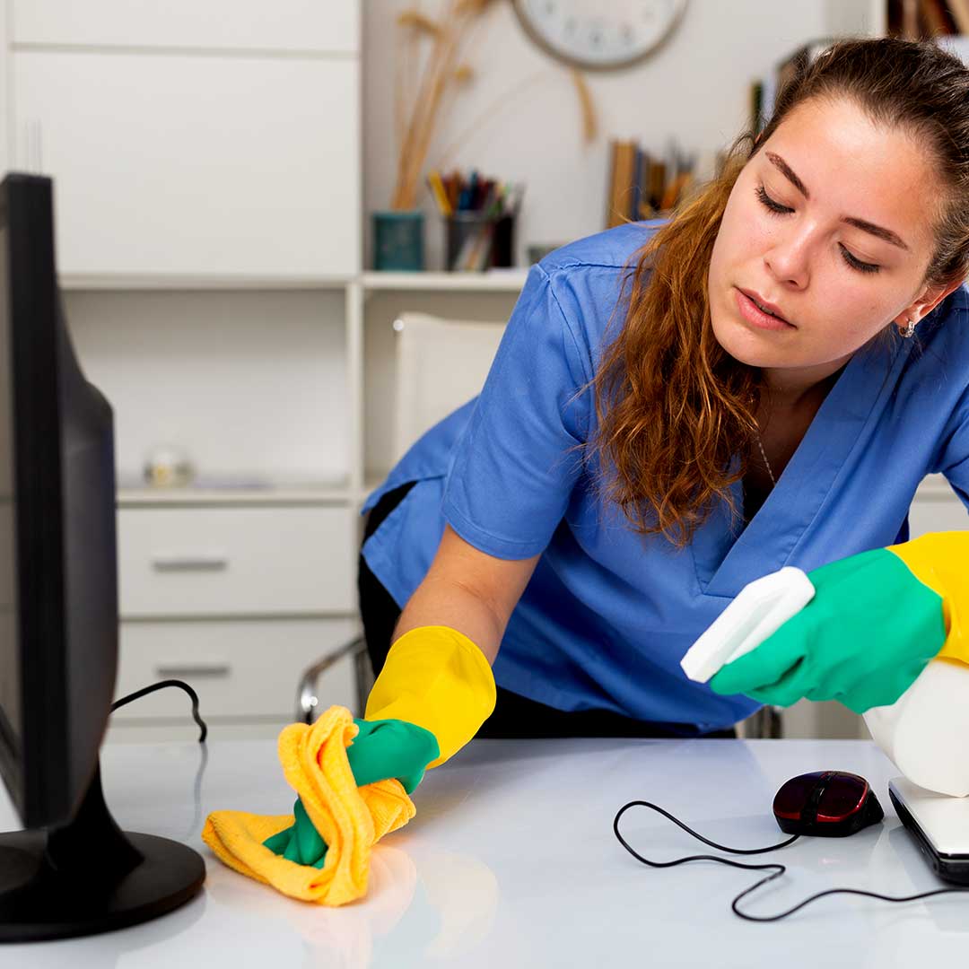 Cleaning professional wearing gloves sanitizing an office desk with a spray bottle and cloth